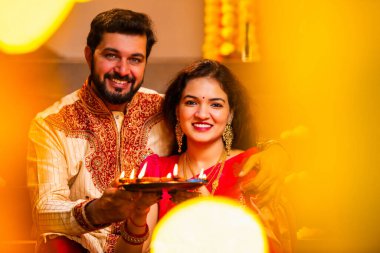 Geleneksel Giyinik Merdivenlerde oturan, terakotta yağı tabağı tutan ve Diwali Festivali Kutlaması sırasında gülümseyen kameraya bakan Hintli çift Diya Thali ile Mutlu Diwali diyetleri diler.