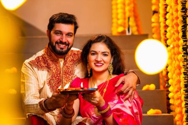 Geleneksel Giyinik Merdivenlerde oturan, terakotta yağı tabağı tutan ve Diwali Festivali Kutlaması sırasında gülümseyen kameraya bakan Hintli çift Diya Thali ile Mutlu Diwali diyetleri diler.