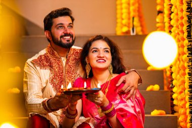 Geleneksel Giyinik Merdivenlerde oturan, terakotta yağı tabağı tutan ve Diwali Festivali Kutlaması sırasında gülümseyen kameraya bakan Hintli çift Diya Thali ile Mutlu Diwali diyetleri diler.