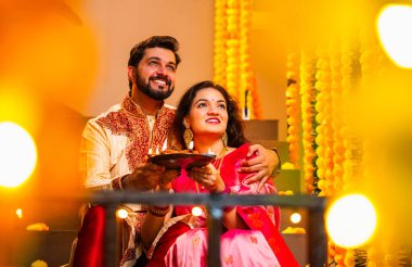 Geleneksel Giyinik Merdivenlerde oturan, terakotta yağı tabağı tutan ve Diwali Festivali Kutlaması sırasında gülümseyen kameraya bakan Hintli çift Diya Thali ile Mutlu Diwali diyetleri diler.