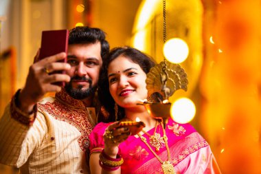 Selfie Aydınlatma Diwali Samai, Saree 'deki Hintli Evli Çift ve Kurta Geleneksel Pirinç Yağı Lambası ile Bayram Gecesini Kocası Smartphone' da Smartphone 'a Gülümseyerek Selfie Tıkladı