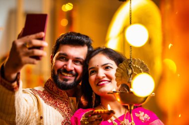 Selfie Aydınlatma Diwali Samai, Saree 'deki Hintli Evli Çift ve Kurta Geleneksel Pirinç Yağı Lambası ile Bayram Gecesini Kocası Smartphone' da Smartphone 'a Gülümseyerek Selfie Tıkladı