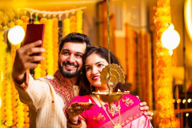 Selfie Aydınlatma Diwali Samai, Saree 'deki Hintli Evli Çift ve Kurta Geleneksel Pirinç Yağı Lambası ile Bayram Gecesini Kocası Smartphone' da Smartphone 'a Gülümseyerek Selfie Tıkladı