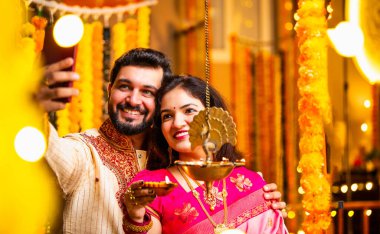 Selfie Aydınlatma Diwali Samai, Saree 'deki Hintli Evli Çift ve Kurta Geleneksel Pirinç Yağı Lambası ile Bayram Gecesini Kocası Smartphone' da Smartphone 'a Gülümseyerek Selfie Tıkladı