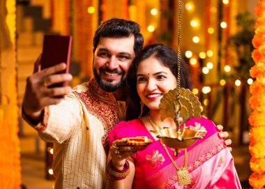 Selfie Aydınlatma Diwali Samai, Saree 'deki Hintli Evli Çift ve Kurta Geleneksel Pirinç Yağı Lambası ile Bayram Gecesini Kocası Smartphone' da Smartphone 'a Gülümseyerek Selfie Tıkladı