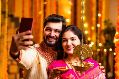 Selfie Aydınlatma Diwali Samai, Saree 'deki Hintli Evli Çift ve Kurta Geleneksel Pirinç Yağı Lambası ile Bayram Gecesini Kocası Smartphone' da Smartphone 'a Gülümseyerek Selfie Tıkladı