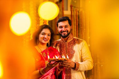 Geleneksel Saree 'deki Hintli evli çift Diya Thali ve Marigold Garland' a Karşı Ayakta Duran, Terracotta Petrol Lambası Tabağı Tutan ve Festivalde Kamerada Gülümseyen