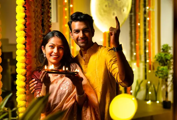 Geleneksel etnik kıyafetli Hintli çift, bayram gecesi Hindu festivali kutlamalarında renkli kadife çiçeklerinin önünde sevinçle dikiliyorlar.