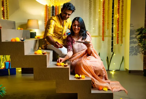 Diwali 'ye merdiven dayayan Hintli çift geleneksel şenlik kıyafetleri içinde geceleri Deepavali kutlamaları için teras lambaları yakıyor. Gülümsüyor, seviniyor ve renkli çle süsleniyor.