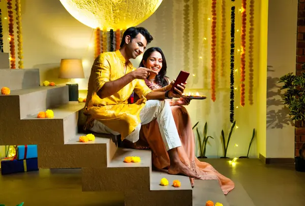 Merdivenlerdeki video görüşmelerine katılan Hintli çift Diwali gecesi kutlamalarında arkadaşlarıyla bağ kuruyor. Dekoratif merdivenlerde Divalar ve çelenklerle oturuyorlar.