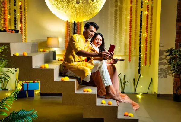 Merdivenlerdeki video görüşmelerine katılan Hintli çift Diwali gecesi kutlamalarında arkadaşlarıyla bağ kuruyor. Dekoratif merdivenlerde Divalar ve çelenklerle oturuyorlar.