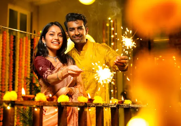 Geleneksel Şenlik Giysileri içinde korkulukların yanında dikilen, Sparkles ve Havai fişeklerle Diwali Gecesinde Neşeli Gülümseyen ve Kutlayan Hintli Çiftler