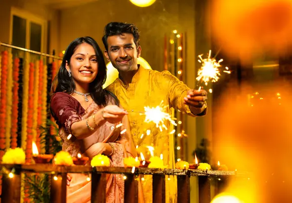 Geleneksel Şenlik Giysileri içinde korkulukların yanında dikilen, Sparkles ve Havai fişeklerle Diwali Gecesinde Neşeli Gülümseyen ve Kutlayan Hintli Çiftler
