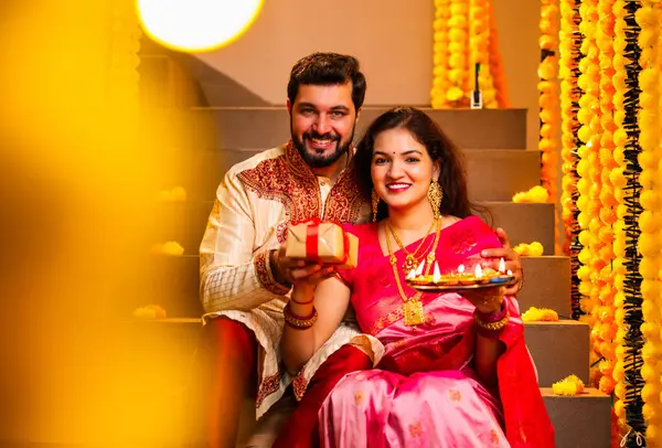 Koca, Karısına Diwali Hediyesi Veriyor, Geleneksel Giysilerle Dekoratif Merdivenlerde oturan Hintli Çift, Diya Thali 'yi tutuyor, Diwali Gecesinde Gülümseyen ve Karşılıklı Sürpriz Hediye Veriyor