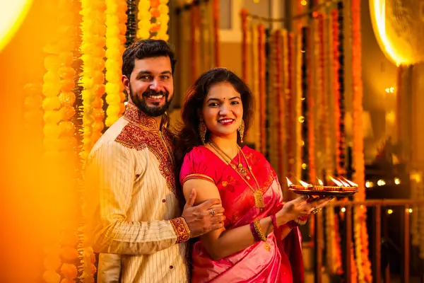 Geleneksel Saree 'deki Hintli evli çift Diya Thali ve Marigold Garland' a Karşı Ayakta Duran, Terracotta Petrol Lambası Tabağı Tutan ve Festivalde Kamerada Gülümseyen