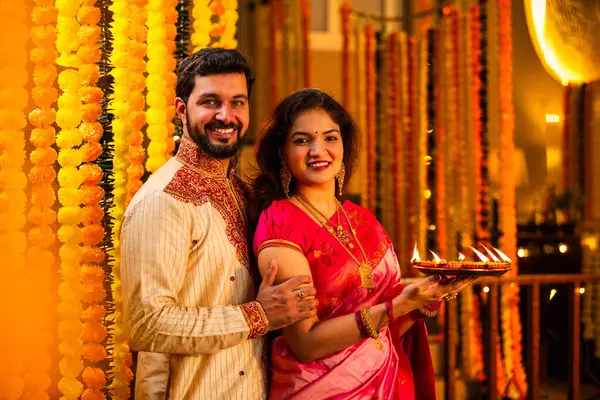 Geleneksel Saree 'deki Hintli evli çift Diya Thali ve Marigold Garland' a Karşı Ayakta Duran, Terracotta Petrol Lambası Tabağı Tutan ve Festivalde Kamerada Gülümseyen