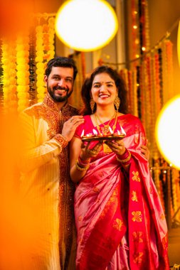 Geleneksel Saree 'deki Hintli evli çift Diya Thali ve Marigold Garland' a Karşı Ayakta Duran, Terracotta Petrol Lambası Tabağı Tutan ve Festivalde Kamerada Gülümseyen
