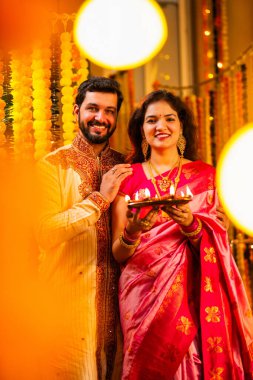 Geleneksel Saree 'deki Hintli evli çift Diya Thali ve Marigold Garland' a Karşı Ayakta Duran, Terracotta Petrol Lambası Tabağı Tutan ve Festivalde Kamerada Gülümseyen