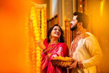 Marigold Garland ile Diwali İçin Dekorasyon, Geleneksel Etnik Giyimli Mutlu Hintli Genç Evli Çift, Hindu Festivali Kutlamaları sırasında İçerde Çiçek Dekorasyonu Yapıyor