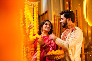 Marigold Garland ile Diwali İçin Dekorasyon, Geleneksel Etnik Giyimli Mutlu Hintli Genç Evli Çift, Hindu Festivali Kutlamaları sırasında İçerde Çiçek Dekorasyonu Yapıyor