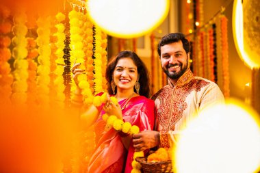 Marigold Garland ile Diwali İçin Dekorasyon, Geleneksel Etnik Giyimli Mutlu Hintli Genç Evli Çift, Hindu Festivali Kutlamaları sırasında İçerde Çiçek Dekorasyonu Yapıyor