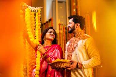 Marigold Garland ile Diwali İçin Dekorasyon, Geleneksel Etnik Giyimli Mutlu Hintli Genç Evli Çift, Hindu Festivali Kutlamaları sırasında İçerde Çiçek Dekorasyonu Yapıyor