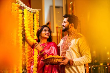 Marigold Garland ile Diwali İçin Dekorasyon, Geleneksel Etnik Giyimli Mutlu Hintli Genç Evli Çift, Hindu Festivali Kutlamaları sırasında İçerde Çiçek Dekorasyonu Yapıyor