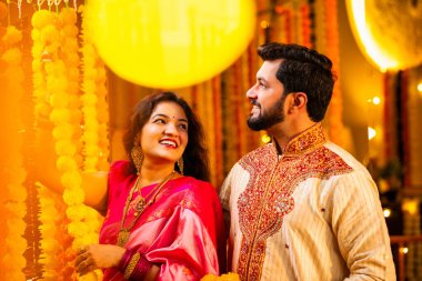 Marigold Garland ile Diwali İçin Dekorasyon, Geleneksel Etnik Giyimli Mutlu Hintli Genç Evli Çift, Hindu Festivali Kutlamaları sırasında İçerde Çiçek Dekorasyonu Yapıyor