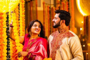 Marigold Garland ile Diwali İçin Dekorasyon, Geleneksel Etnik Giyimli Mutlu Hintli Genç Evli Çift, Hindu Festivali Kutlamaları sırasında İçerde Çiçek Dekorasyonu Yapıyor