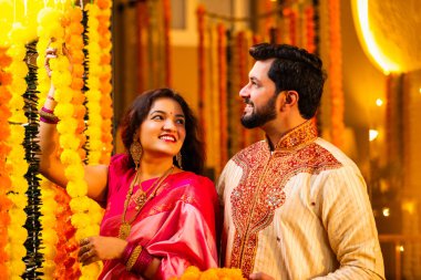 Marigold Garland ile Diwali İçin Dekorasyon, Geleneksel Etnik Giyimli Mutlu Hintli Genç Evli Çift, Hindu Festivali Kutlamaları sırasında İçerde Çiçek Dekorasyonu Yapıyor