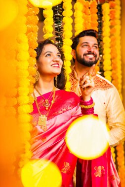 Etnik Giyimli Kadın ve Erkek Marigold Garland Duvarı 'nı aşıyor ve Diwali Kutlaması sırasında yukarı bakarken şaşkınlıkla reaksiyon gösteriyor.