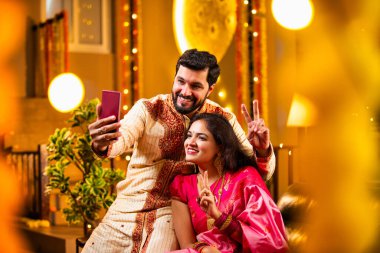 Diwali Video Call 'dan dilek diliyor. Geleneksel Etnik Giyimli Hintli genç çift Diwali Festivali 'nde Işık ve Şölen Dekorasyonu' nda Akrabaları bağlamak için akıllı telefonu kullanıyor