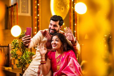 Diwali Video Call 'dan dilek diliyor. Geleneksel Etnik Giyimli Hintli genç çift Diwali Festivali 'nde Işık ve Şölen Dekorasyonu' nda Akrabaları bağlamak için akıllı telefonu kullanıyor