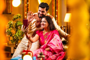 Diwali Video Call 'dan dilek diliyor. Geleneksel Etnik Giyimli Hintli genç çift Diwali Festivali 'nde Işık ve Şölen Dekorasyonu' nda Akrabaları bağlamak için akıllı telefonu kullanıyor