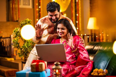 Diwali Video Call 'dan dilek diliyor. Geleneksel Etnik Giyimli Hintli genç çift Diwali Festivali 'nde Işık ve Şenlik Dekorasyonu' nda Akrabaları bağlamak için dizüstü bilgisayar kullanıyor