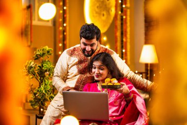 Diwali Video Call 'dan dilek diliyor. Geleneksel Etnik Giyimli Hintli genç çift Diwali Festivali 'nde Işık ve Şenlik Dekorasyonu' nda Akrabaları bağlamak için dizüstü bilgisayar kullanıyor