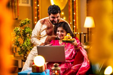 Diwali Video Call 'dan dilek diliyor. Geleneksel Etnik Giyimli Hintli genç çift Diwali Festivali 'nde Işık ve Şenlik Dekorasyonu' nda Akrabaları bağlamak için dizüstü bilgisayar kullanıyor
