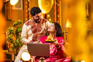 Diwali Video Call 'dan dilek diliyor. Geleneksel Etnik Giyimli Hintli genç çift Diwali Festivali 'nde Işık ve Şenlik Dekorasyonu' nda Akrabaları bağlamak için dizüstü bilgisayar kullanıyor