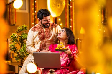 Diwali Video Call 'dan dilek diliyor. Geleneksel Etnik Giyimli Hintli genç çift Diwali Festivali 'nde Işık ve Şenlik Dekorasyonu' nda Akrabaları bağlamak için dizüstü bilgisayar kullanıyor