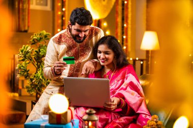 Online Diwali Alışveriş yapmak Laptop ve Kredi Kartı kullanmak. Geleneksel Etnik Giyimli Şenlik Kutlamaları sırasında Tatlılarla Süslü Ev 'de oturan Hintli genç çift