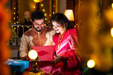 Açılış Parlayan Hediye Kutusu, Tatlılar ve Hediyelerle çevrili, Evde Diwali Festivali 'ni kutlayan Hintli genç çift, Kutudan çıkan parıltıyla şaşırdılar.