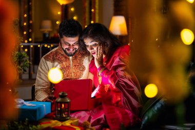 Açılış Parlayan Hediye Kutusu, Tatlılar ve Hediyelerle çevrili, Evde Diwali Festivali 'ni kutlayan Hintli genç çift, Kutudan çıkan parıltıyla şaşırdılar.