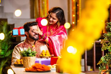 Geleneksel Şenlik Giysileriyle Evde Otururken, Evde Işıklar ve Marigold çelenkleriyle süslenmiş Diwali Gecesini Gülümseyen ve Kutlayan Hintli Eş Kocaya Sürpriz Hediye Veriyor