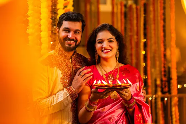 Geleneksel Saree 'deki Hintli evli çift Diya Thali ve Marigold Garland' a Karşı Ayakta Duran, Terracotta Petrol Lambası Tabağı Tutan ve Festivalde Kamerada Gülümseyen