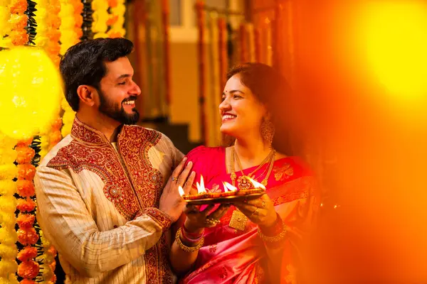 Geleneksel Saree 'deki Hintli evli çift Diya Thali ve Marigold Garland' a Karşı Ayakta Duran, Terracotta Petrol Lambası Tabağı Tutan ve Festivalde Kamerada Gülümseyen