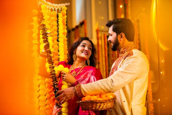 Marigold Garland ile Diwali İçin Dekorasyon, Geleneksel Etnik Giyimli Mutlu Hintli Genç Evli Çift, Hindu Festivali Kutlamaları sırasında İçerde Çiçek Dekorasyonu Yapıyor