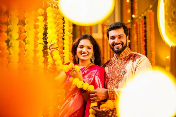 Marigold Garland ile Diwali İçin Dekorasyon, Geleneksel Etnik Giyimli Mutlu Hintli Genç Evli Çift, Hindu Festivali Kutlamaları sırasında İçerde Çiçek Dekorasyonu Yapıyor