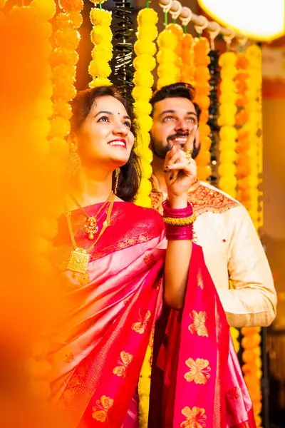 Etnik Giyimli Kadın ve Erkek Marigold Garland Duvarı 'nı aşıyor ve Diwali Kutlaması sırasında yukarı bakarken şaşkınlıkla reaksiyon gösteriyor.