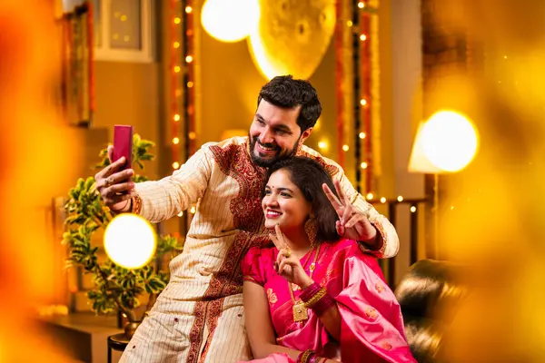 Diwali Video Call 'dan dilek diliyor. Geleneksel Etnik Giyimli Hintli genç çift Diwali Festivali 'nde Işık ve Şölen Dekorasyonu' nda Akrabaları bağlamak için akıllı telefonu kullanıyor