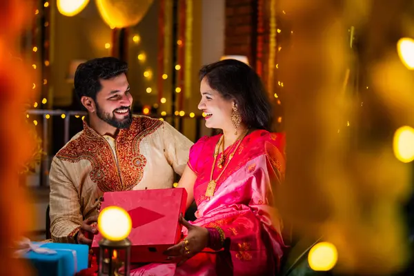 Açılış Parlayan Hediye Kutusu, Tatlılar ve Hediyelerle çevrili, Evde Diwali Festivali 'ni kutlayan Hintli genç çift, Kutudan çıkan parıltıyla şaşırdılar.